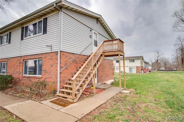 view of side of property featuring a lawn, brick siding, a wooden deck, and stairs