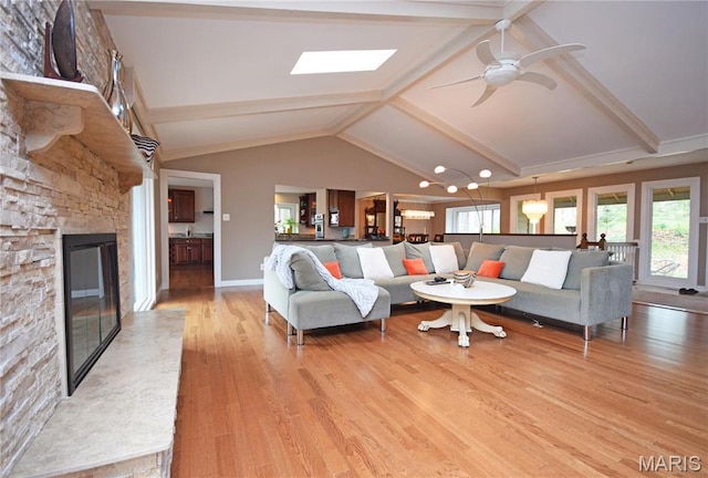 living area with light wood-style flooring, a ceiling fan, a stone fireplace, beam ceiling, and baseboards