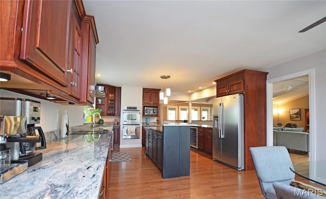 kitchen with stainless steel appliances, a ceiling fan, a center island, light wood-type flooring, and beverage cooler