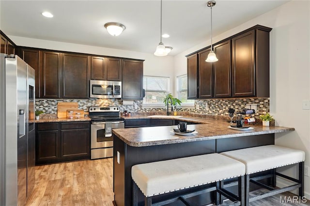 1914 Teresa Fields Ln, Lake St Louis, MO 63367 - kitchen featuring appliances with stainless steel finishes, a peninsula, dark brown cabinets, a sink, and tasteful backsplash