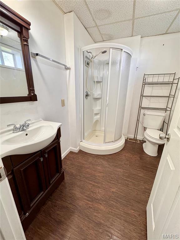 1001 S Central Ave, Vandalia, MO 63382 - full bathroom with baseboards, a stall shower, wood finished floors, a drop ceiling, and toilet