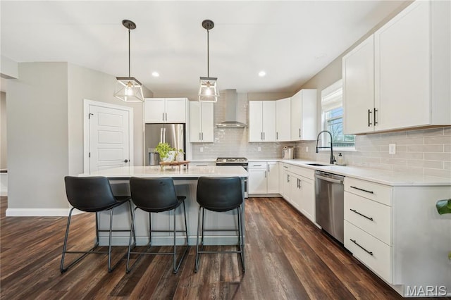 kitchen with a sink, wall chimney range hood, appliances with stainless steel finishes, a kitchen breakfast bar, and decorative backsplash