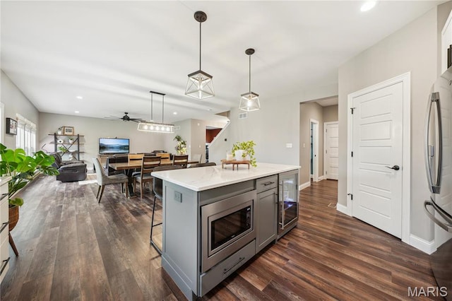 kitchen with gray cabinetry, appliances with stainless steel finishes, beverage cooler, a breakfast bar area, and dark wood-type flooring