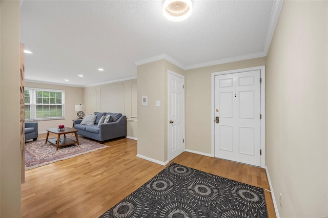 entrance foyer featuring light wood-type flooring, ornamental molding, baseboards, a textured ceiling, and recessed lighting