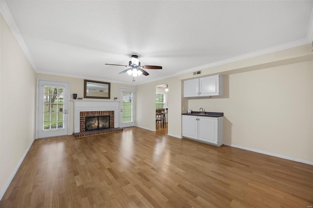 unfurnished living room with a sink, a ceiling fan, light wood-type flooring, baseboards, and ornamental molding