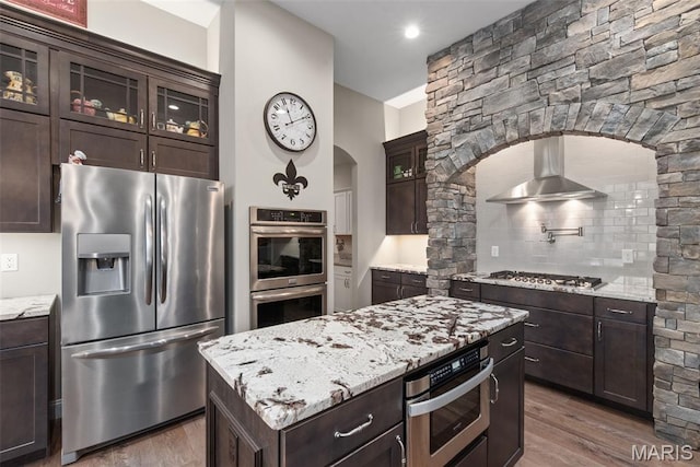 408 Hamlet Ct, Lake St Louis, MO 63367 - kitchen featuring stainless steel appliances, arched walkways, range hood, wood finished floors, and light stone counters