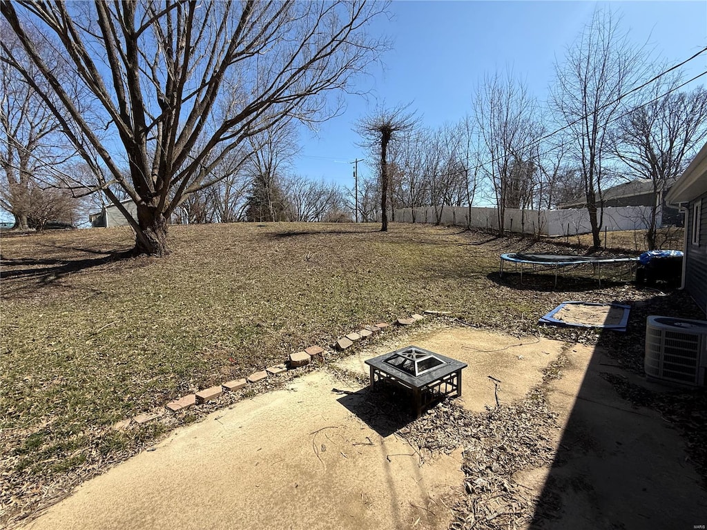 view of yard featuring a trampoline, a fire pit, cooling unit, and fence