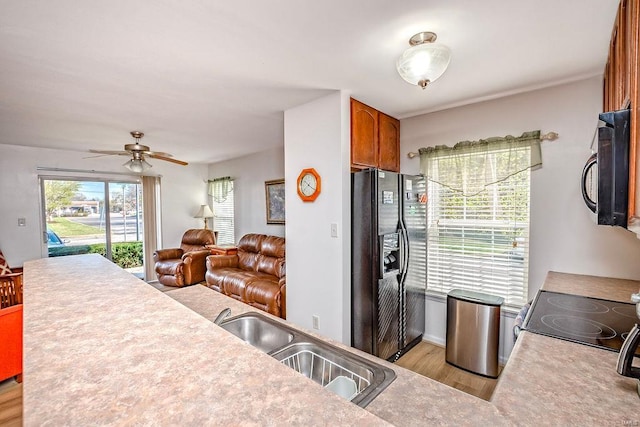 kitchen featuring black appliances, a sink, light wood-type flooring, open floor plan, and brown cabinetry