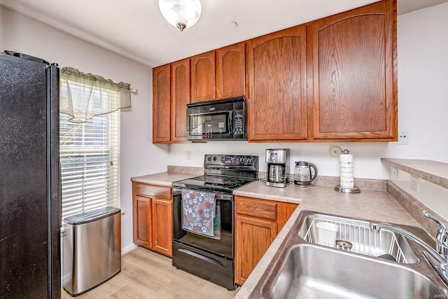 kitchen with black appliances, a sink, light wood-type flooring, light countertops, and brown cabinetry