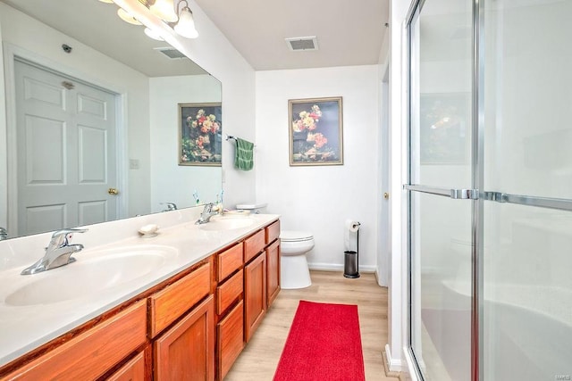bathroom featuring a stall shower, wood finished floors, double vanity, toilet, and baseboards