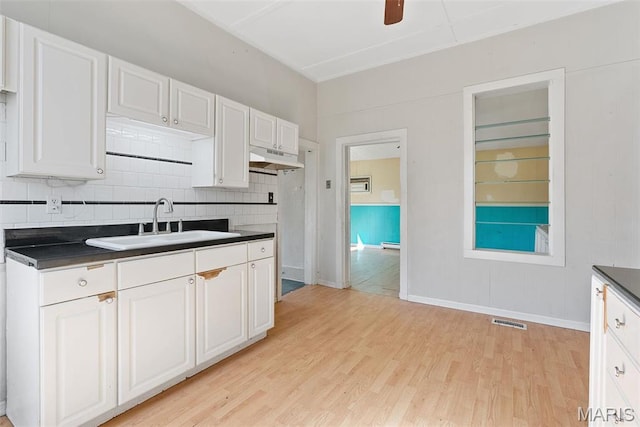 104 S 4th St, De Soto, MO 63020 - kitchen featuring dark countertops, light wood finished floors, white cabinets, and under cabinet range hood