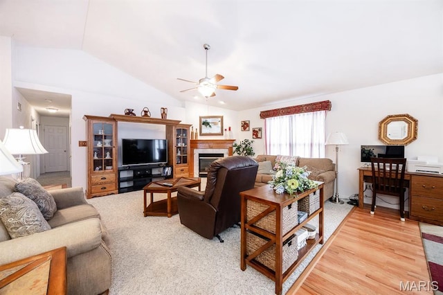 living area with vaulted ceiling, a ceiling fan, and a fireplace