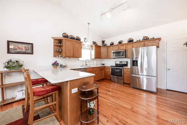 kitchen with appliances with stainless steel finishes, a peninsula, rail lighting, open shelves, and a breakfast bar area