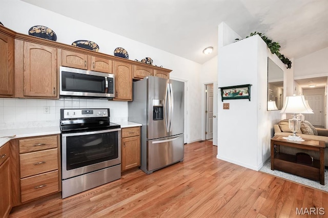 kitchen featuring stainless steel appliances, lofted ceiling, light countertops, light wood finished floors, and decorative backsplash