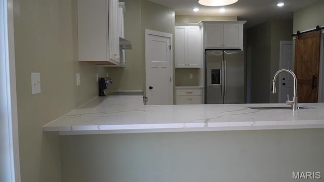 kitchen with stainless steel fridge with ice dispenser, a sink, stove, a barn door, and light stone counters
