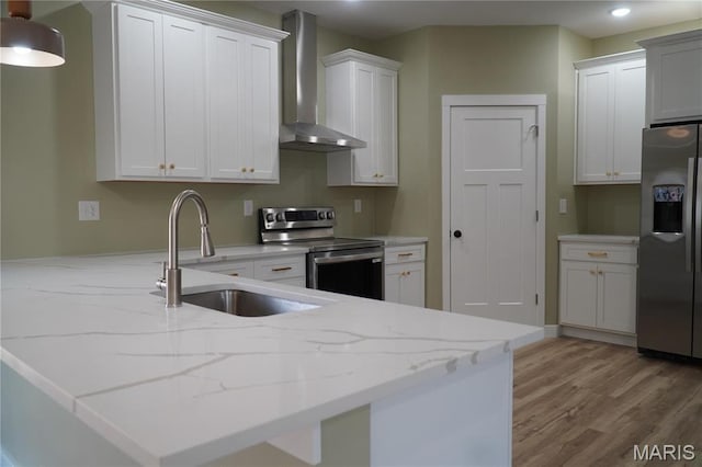 kitchen with stainless steel appliances, wall chimney exhaust hood, a sink, light wood-style flooring, and light stone counters