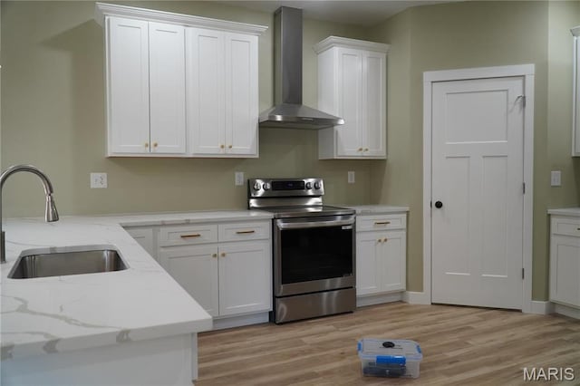 kitchen with stainless steel electric range, wall chimney exhaust hood, a sink, light wood-style floors, and white cabinets