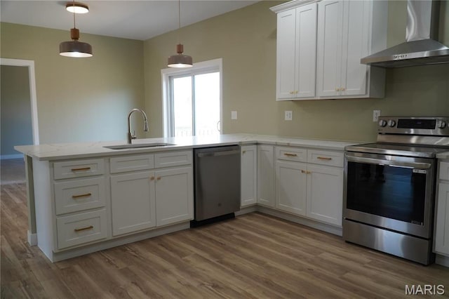kitchen with stainless steel appliances, wall chimney exhaust hood, a sink, a peninsula, and light wood finished floors