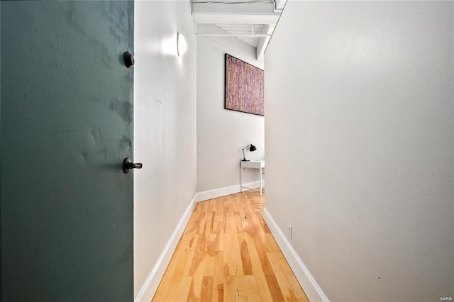 hallway featuring light wood-style flooring, baseboards, and beamed ceiling