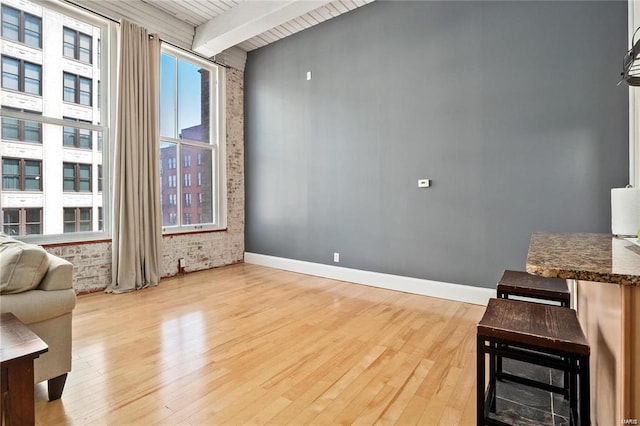 living area with beam ceiling, light wood-style flooring, baseboards, and wooden ceiling