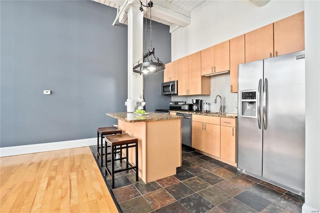 kitchen featuring appliances with stainless steel finishes, a towering ceiling, a sink, beam ceiling, and a kitchen bar