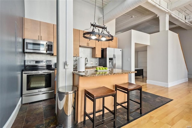 kitchen with stainless steel appliances, a sink, baseboards, a kitchen bar, and beam ceiling