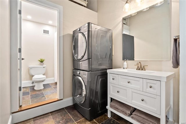 laundry room featuring estacked washer and dryer, stone tile flooring, and baseboards