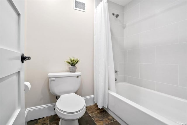 bathroom featuring stone finish floors, toilet, baseboards, and shower / tub combo