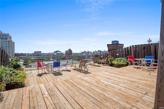 wooden terrace with outdoor dining area, fence, and a view of city