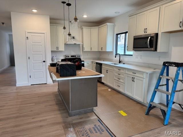kitchen with stainless steel appliances, light wood finished floors, light countertops, a sink, and a center island