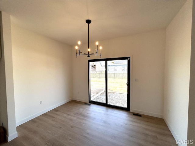 unfurnished dining area with wood finished floors, a chandelier, and baseboards