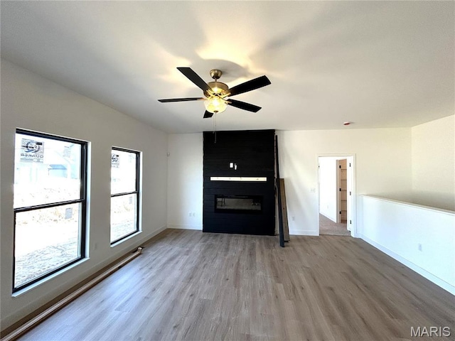 unfurnished living room with a large fireplace, light wood-style flooring, ceiling fan, and baseboards