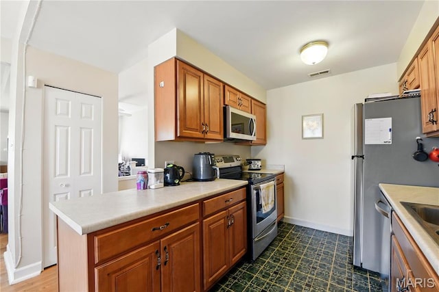 kitchen featuring appliances with stainless steel finishes, light countertops, dark flooring, brown cabinets, and baseboards