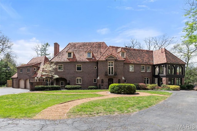 8 Carrswold Dr, Clayton, MO 63105 - tudor house with a chimney, an attached garage, a front yard, driveway, and brick siding