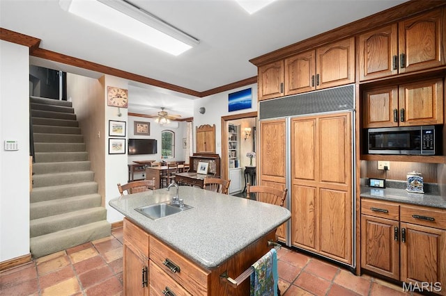 8 Carrswold Dr, Clayton, MO 63105 - kitchen featuring paneled refrigerator, stainless steel microwave, brown cabinets, a sink, and an island with sink