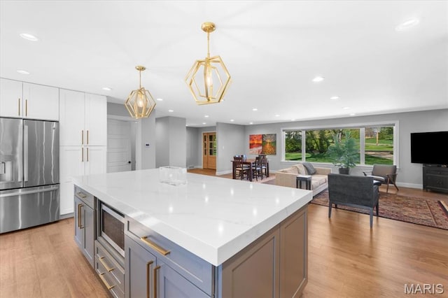 12 Westfield, Frontenac, MO 63131 - kitchen with appliances with stainless steel finishes, open floor plan, light wood-style flooring, white cabinetry, and a kitchen island