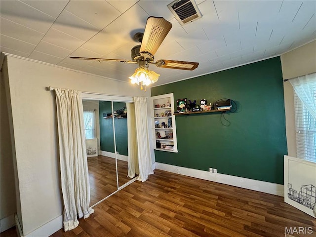 unfurnished bedroom featuring baseboards, wood finished floors, a closet, ceiling fan, and crown molding