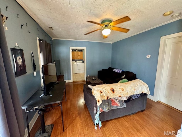 bedroom with washer and clothes dryer, ornamental molding, wood finished floors, a ceiling fan, and baseboards