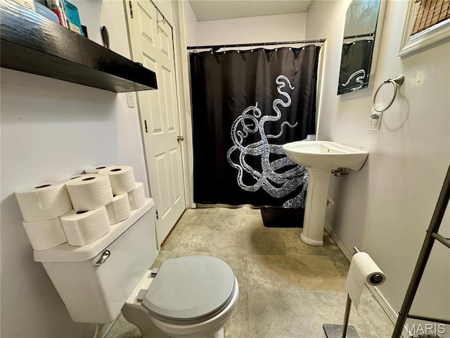 bathroom featuring toilet, baseboards, curtained shower, and stone finish floors