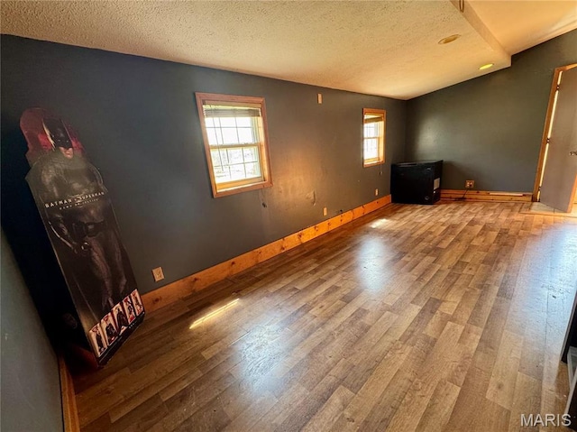 spare room with wood finished floors, a textured ceiling, and baseboards