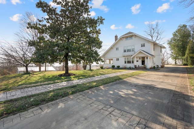 view of front of home featuring concrete driveway, a chimney, and a front lawn