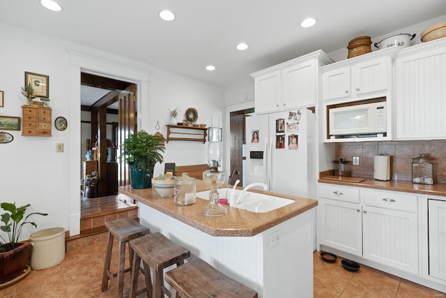 kitchen featuring white appliances, decorative backsplash, light tile patterned flooring, white cabinetry, and a kitchen breakfast bar