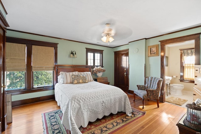 bedroom featuring ornamental molding, hardwood / wood-style floors, baseboards, ensuite bath, and a ceiling fan