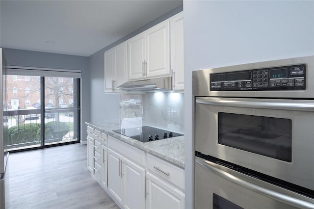 572 Coeur De Royale Dr Unit 108, Saint Louis, MO 63141 - kitchen with black electric cooktop, under cabinet range hood, white cabinetry, light stone counters, and backsplash