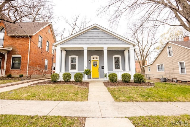 neoclassical home with a porch, cooling unit, and a front lawn
