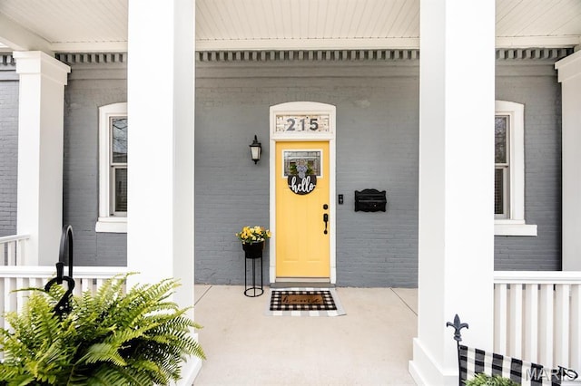 view of exterior entry featuring a porch and brick siding