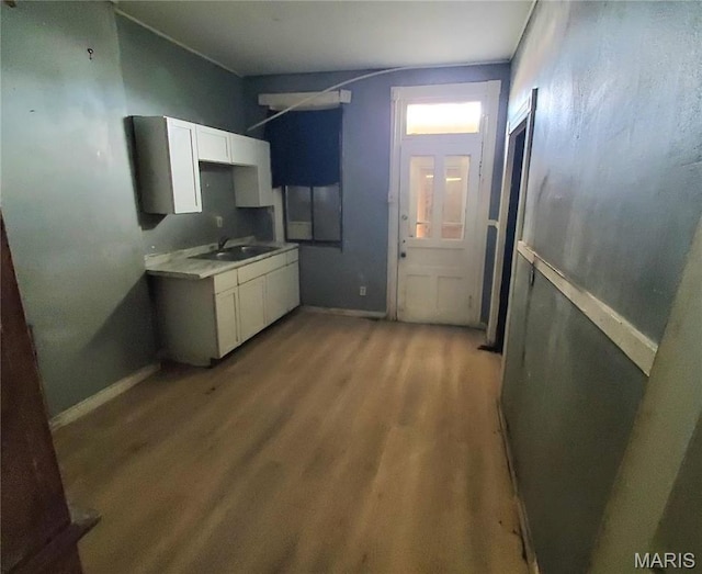 kitchen featuring light wood-type flooring, a sink, white cabinetry, baseboards, and light countertops