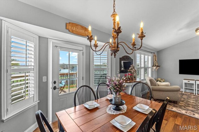dining area with wood finished floors, vaulted ceiling, and a chandelier