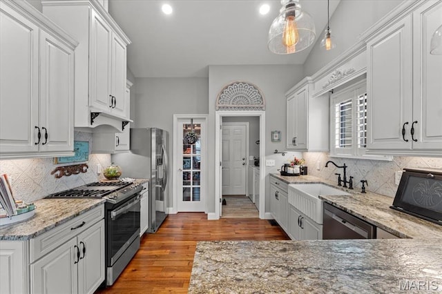 kitchen featuring appliances with stainless steel finishes, white cabinetry, wood finished floors, light stone countertops, and tasteful backsplash