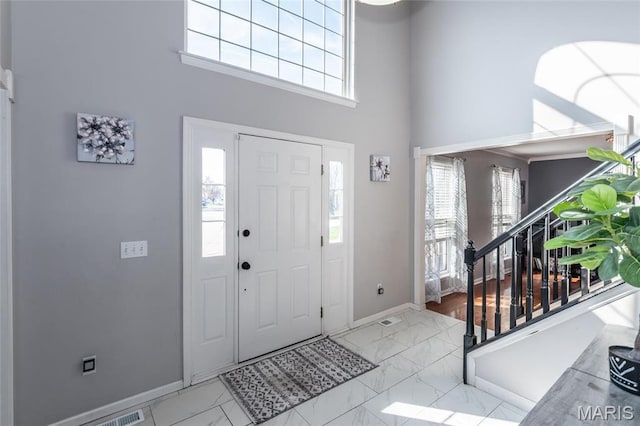 foyer featuring a high ceiling, marble finish floors, stairway, baseboards, and healthy amount of natural light